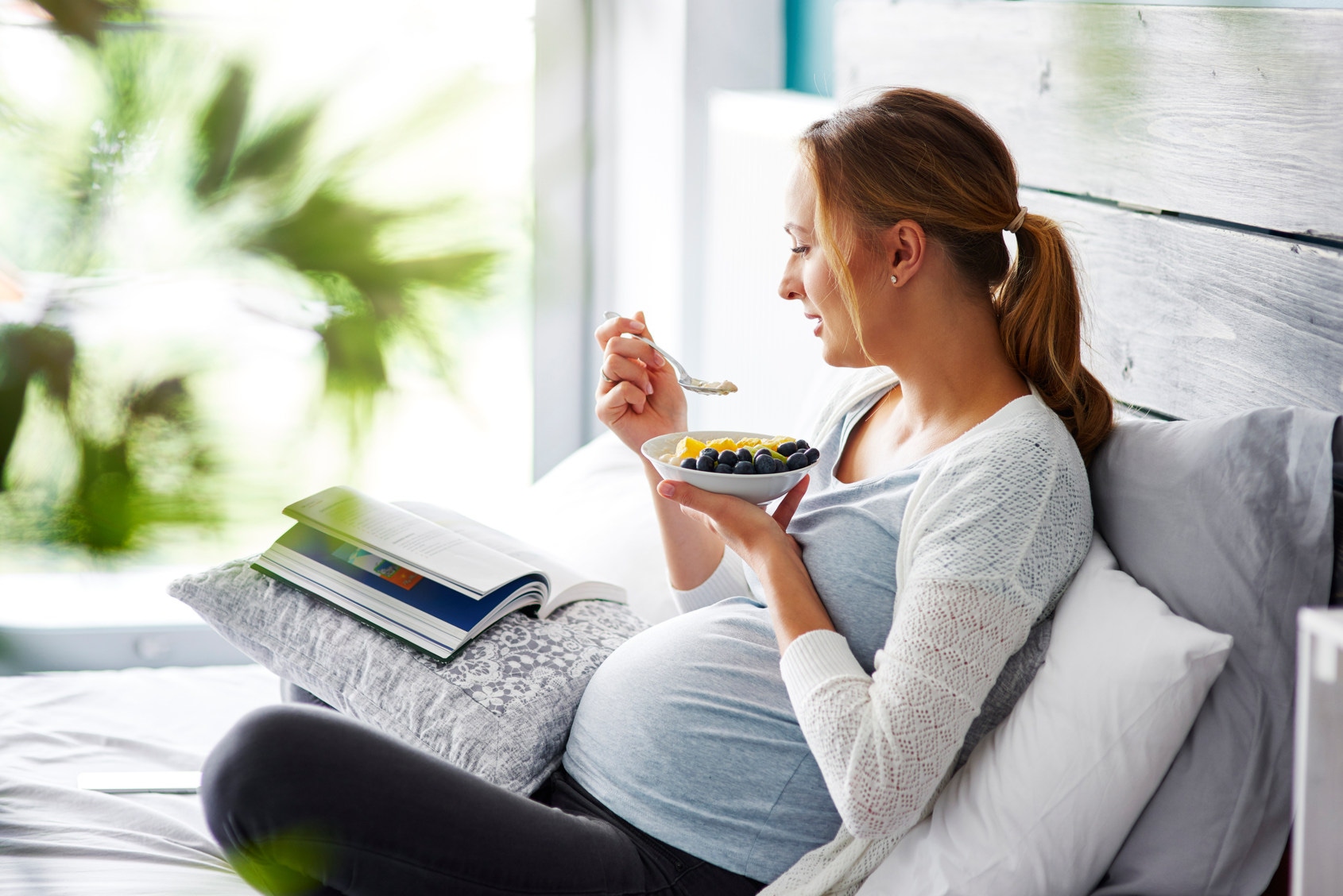 Mujer embarazada comiendo mientras lee un libro 