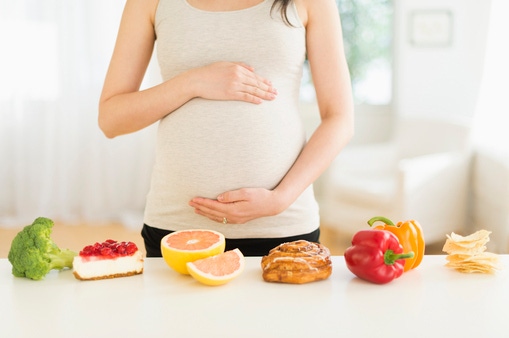 Mujer embarazada con una mesa de alimentos variados al frente 